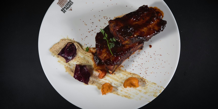 Barbeque ribs saucy meat sprinkled with sesame seeds served on a white plate and signage