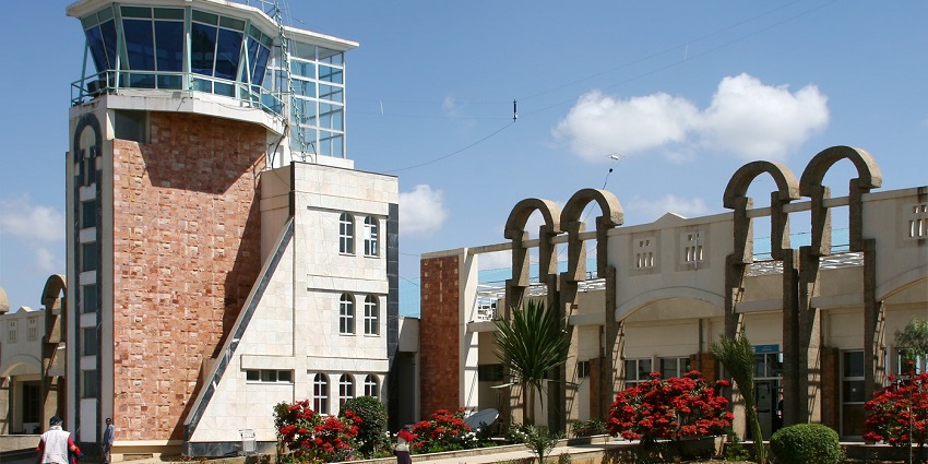 Axum Airport entrance with a passenger pulling a trolley and vibrant red trees outside