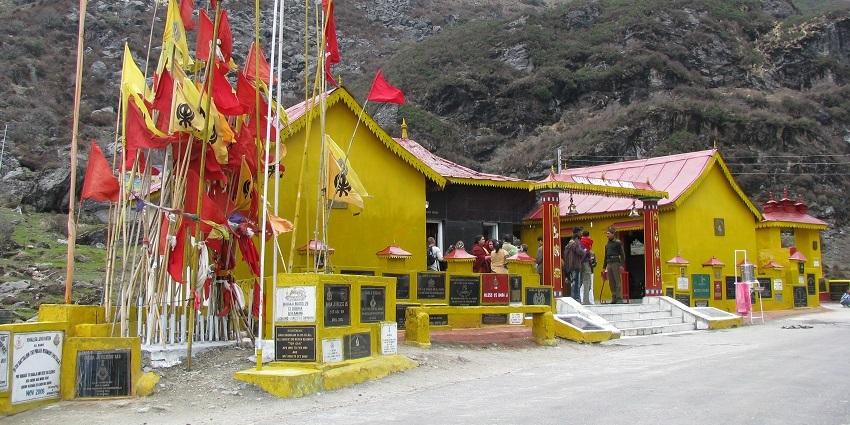 Baba Harbhajan Singh temple with yellow, saffron flags, devotees visiting and mountains.