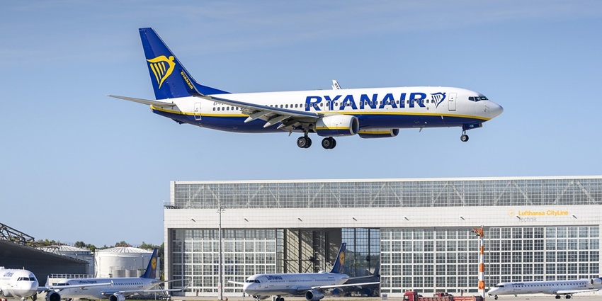 A plane with Ryanair written on it taking off above the glass panels of the airport