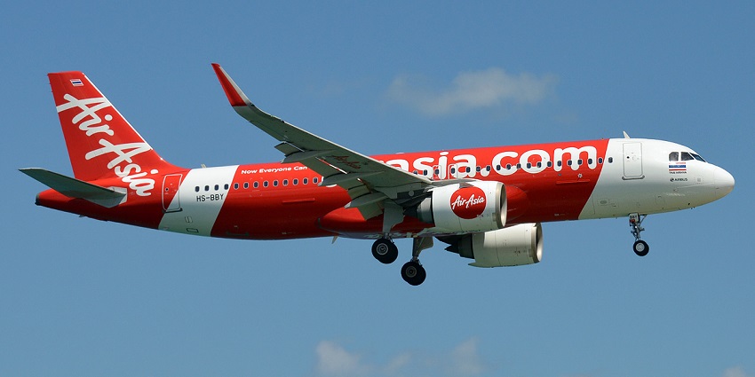 An AirAsia Airbus A320 aircraft with red and white livery flying under a clear blue sky