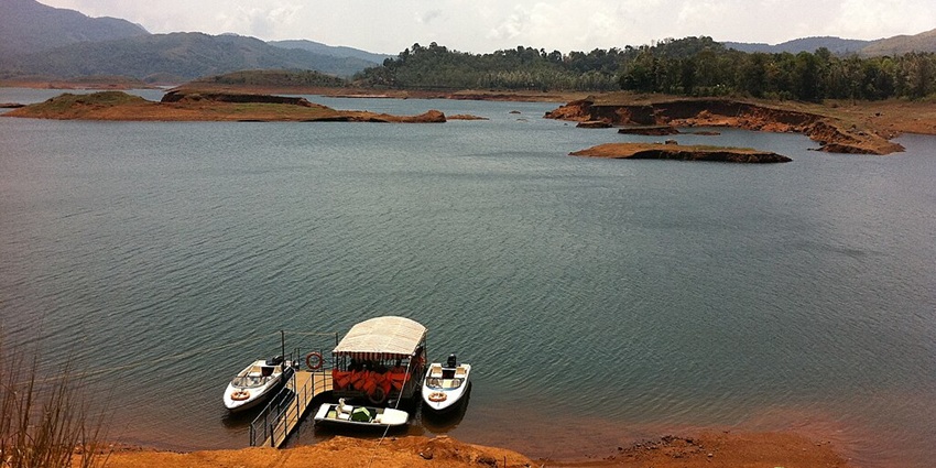 Different boats parked near the shore of Banasura Sagar Dam with sandy shorelines