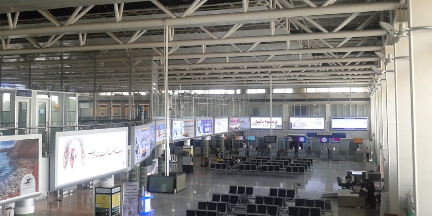 An airplane of IranAir parked on the tarmac in Bandar Abbas Airport with a tower and terminal building.