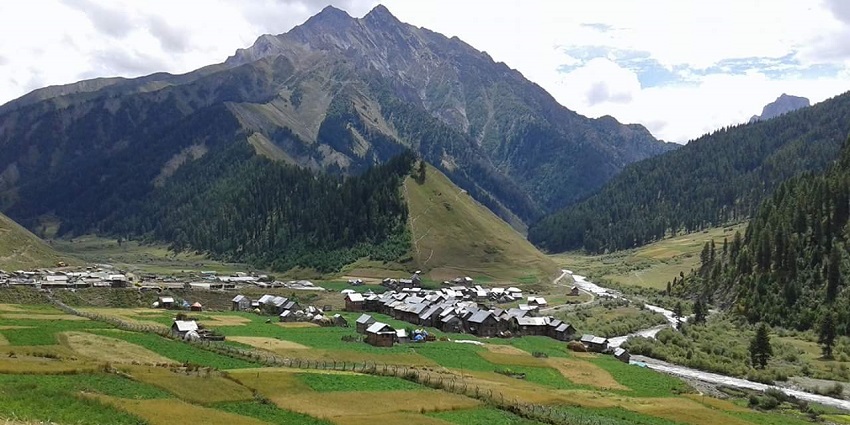 Small village with houses, the river flowing through the greenery and the mountains
