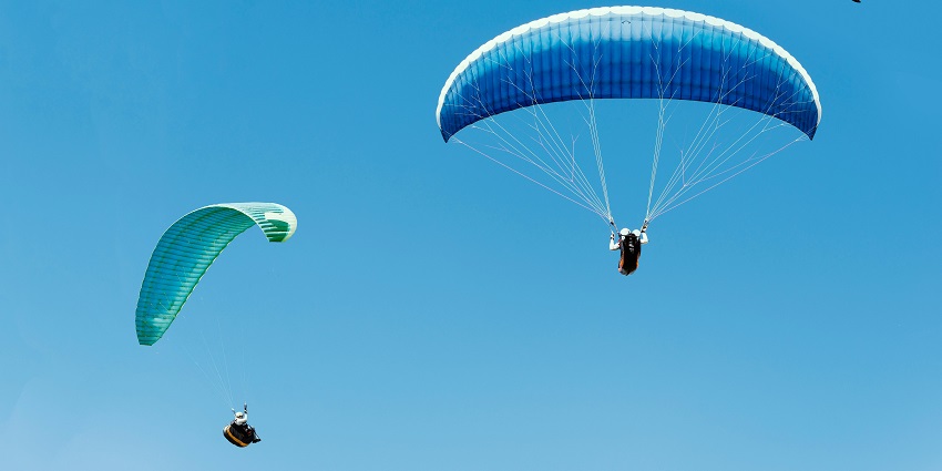 An image of three paragliders with parachutes soaring in a clear blue sky, enjoying the adventure.