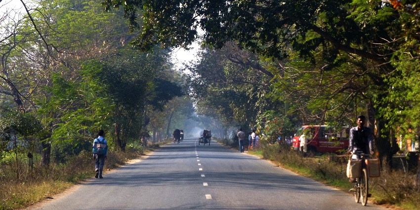Street in Bihar with a man on a bicycle, distant vehicles and people walking on the sides