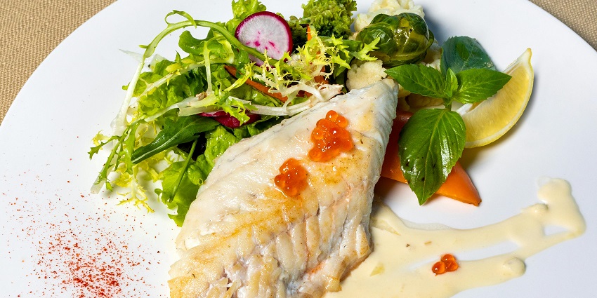 Cooked white barramundi fish dish with green vegetables, lemon and different sauces