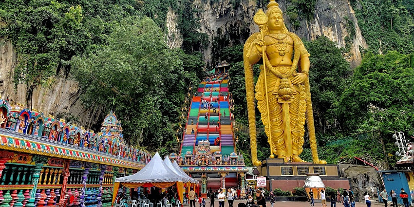 Golden statue stands tall as visitors climb the colourful Batu Cave stairs in the blue sky