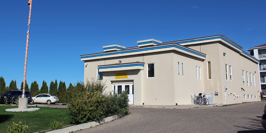 Gurudwara with modern architecture, yellow signage on the entrance and a tall sikh flag