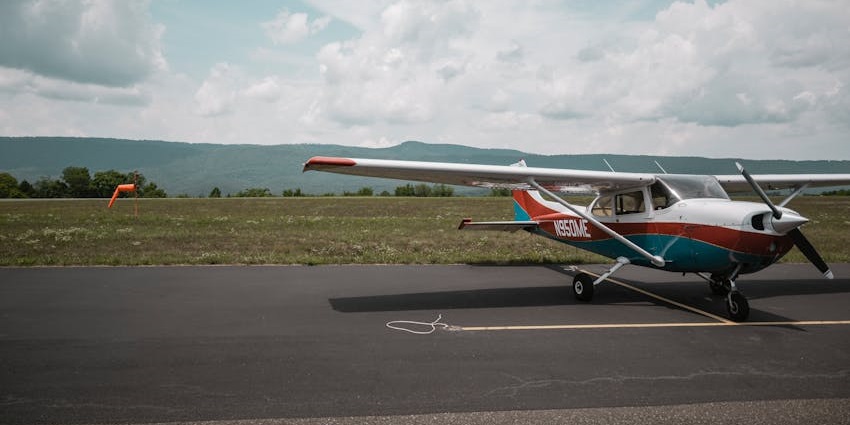 A stretch of runway with a small, private plane parked on it and white clouds above.