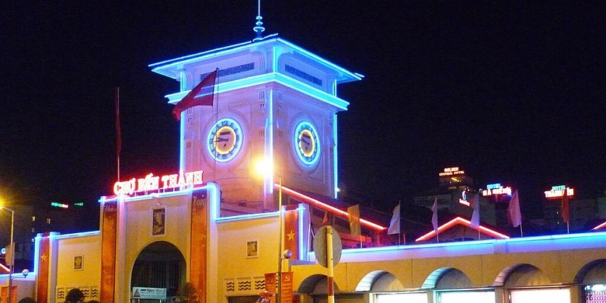 An image showing the southern gate of Ben Thanh Market lit up with colourful lights at night.