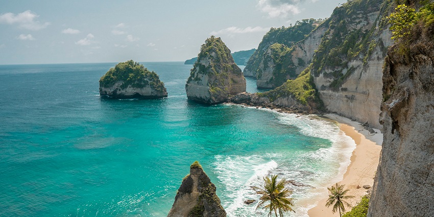 Sunny weather in Nusa Penida with clear blue skies, calm ocean waters, and lush green cliffs during the dry season.