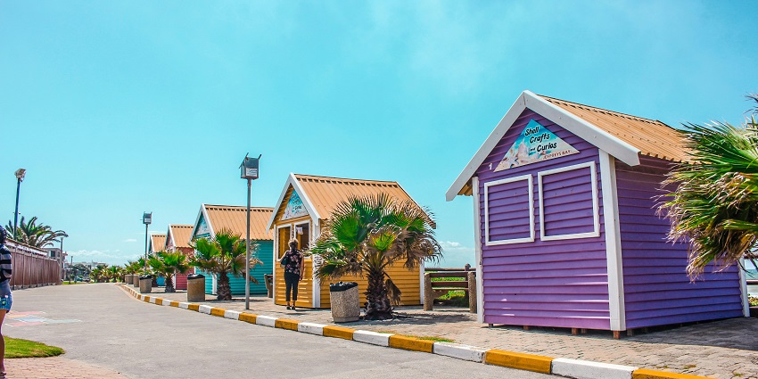 An image of serene Jeffreys Bay with a row of colourful huts next to the ocean.