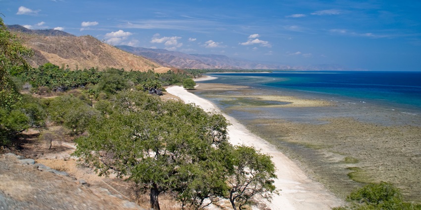 Scenic coastal landscape with a sandy beach, clear blue waters, and distant mountains