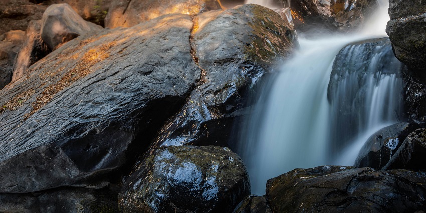 An image of a small, silky waterfall flowing over smooth dark rocks at Sutherland Falls.