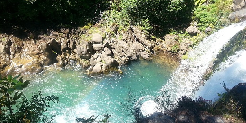 A stunning day at Tawhai Falls, with a clear sky and lush greenery surrounding the waterfall.