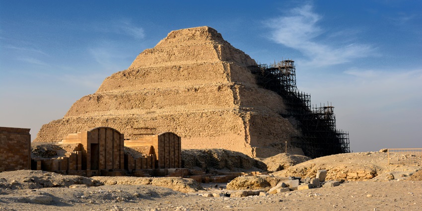 An image of the Pyramid of Djoser bathed in the warm glow of sunrise, with the desert in the background.