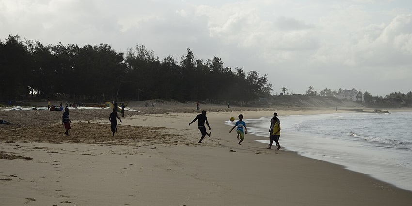 Tofo beach with multiple kids playing football on the sandy shoreline and trees in the back