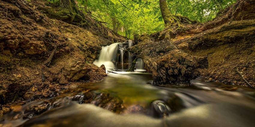 A pristine waterfall standing tall against a vibrant spring sky with blooming greenery.