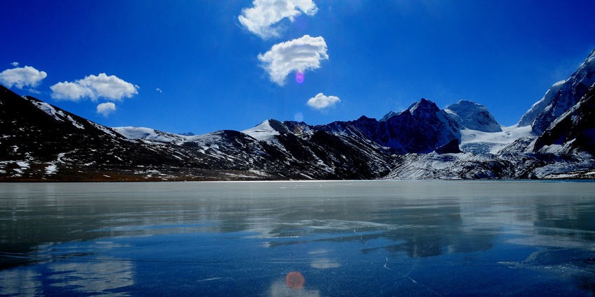 Stunning surroundings of Gurudongmar Lake in December, with snow-capped mountains in the historical past beneath a blue sky.