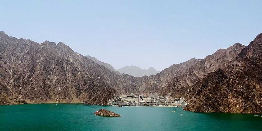 Turquoise waters of Hatta Dam surrounded by rugged mountains under clear blue sky