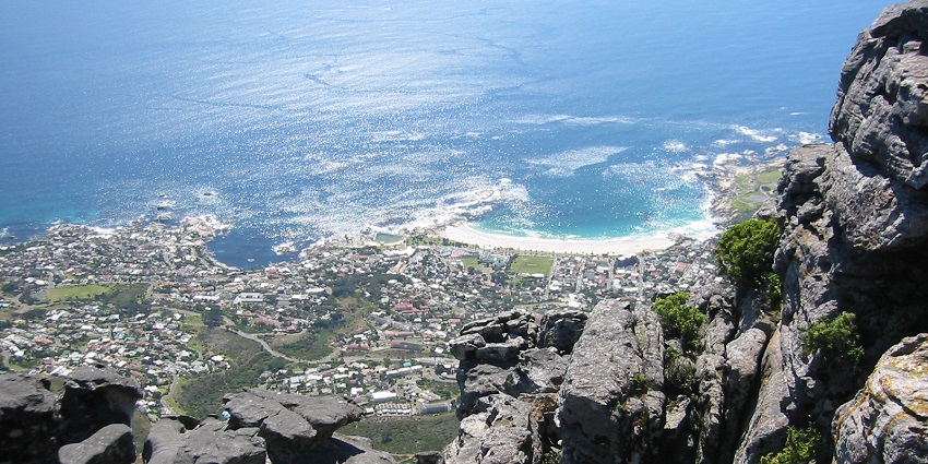An image of Camps Bay Beach, with sparkling ocean views, surrounded by rugged greenery, seen from the summit of Table Mountain.