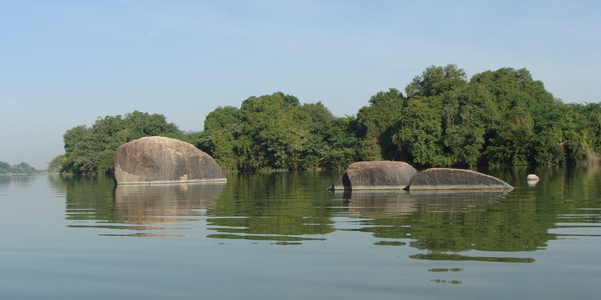 Lake with a vast water expanse reflecting the sky and big rocks, surrounded by greenery