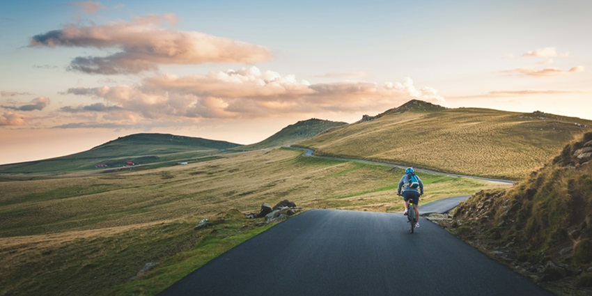 A person, cycling over a trail between the serene surroundings and lush green hills