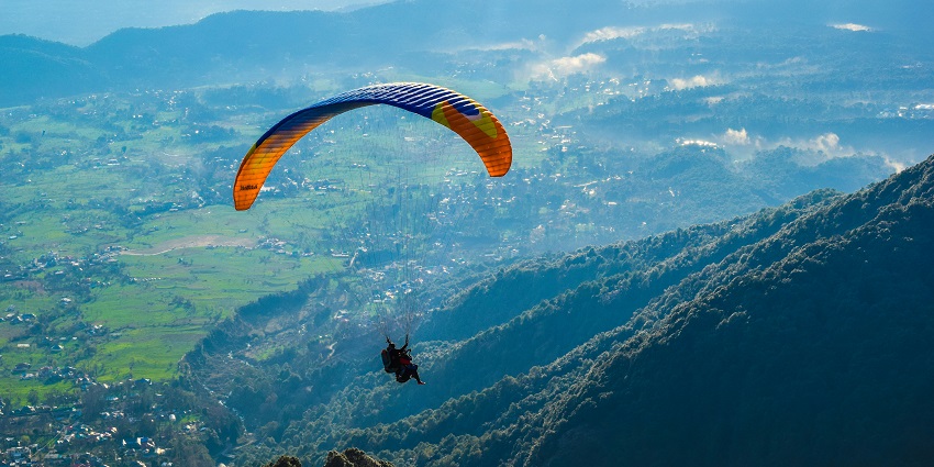 A paraglider in the sky above a grassy field in Bir Billing, Himachal Pradesh, India.