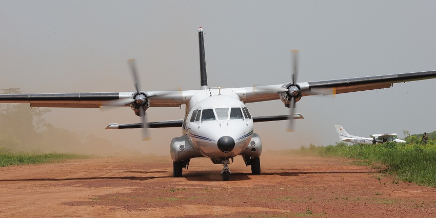 A propeller aircraft landing on a sandy airstrip and another aeroplane in the back