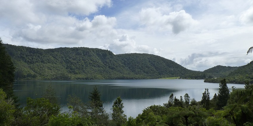 A view of Blue Lake, surrounded by green forests, with its calm waters reflecting the sky.