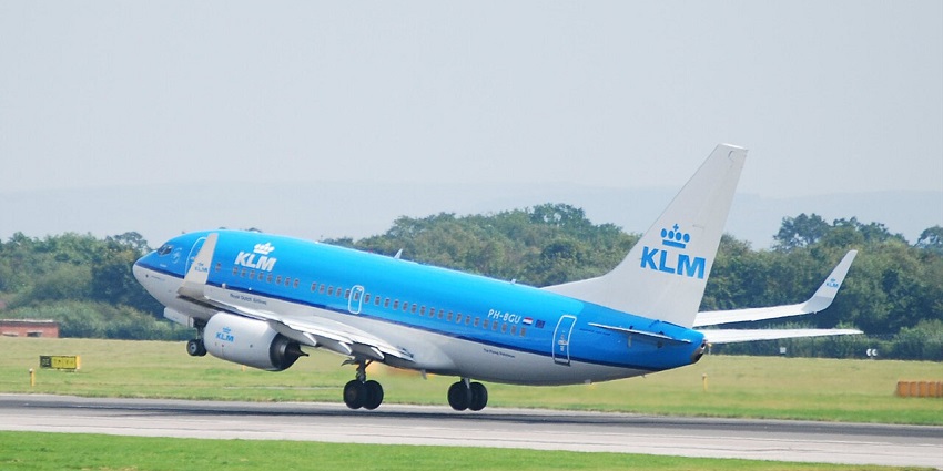 A light blue and white aeroplane taking off from the runway at an airport with greenery