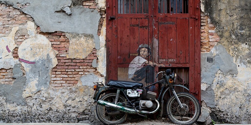 A lifelike 3D street art piece in Penang depicting a curious boy on a real motorbike.