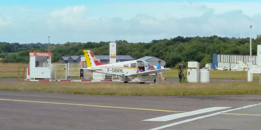 Small propeller aircraft parked on an airstrip and a man standing next to the aircraft