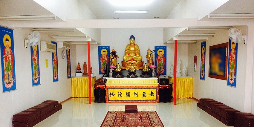 Interior of a Buddhist temple with multiple carpets on the floor and golden statues.