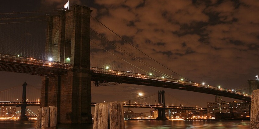 A night view of scenic Brooklyn Bridge with intermittent clouds hovering in the sky.