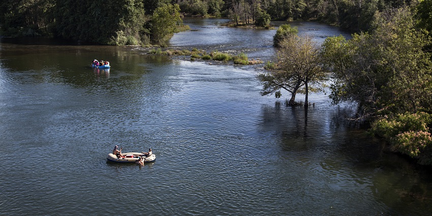 An aerial view of a lake with blue waters, two paddle boats with people in them and trees around