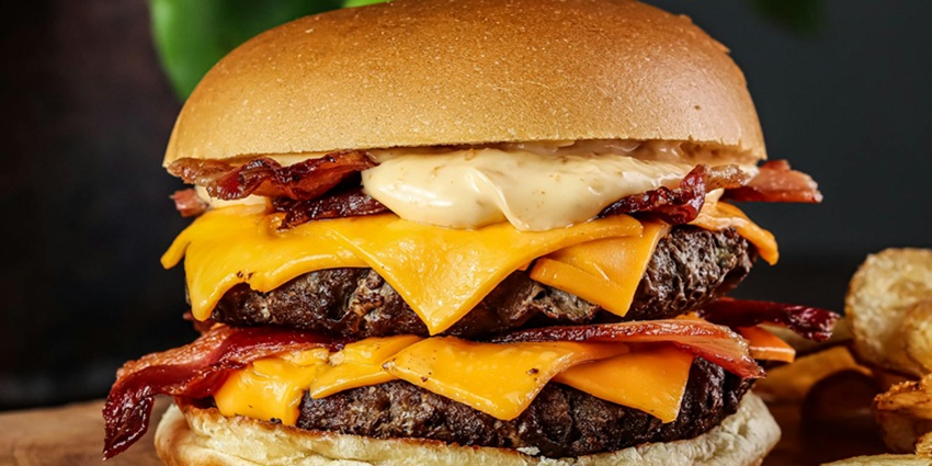 An image of a burger filled with cheese, lettuce, and tomato, a famous food in the USA.