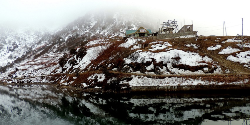 Changu Lake with a small water body, a distant ropeway building and snowy mountains