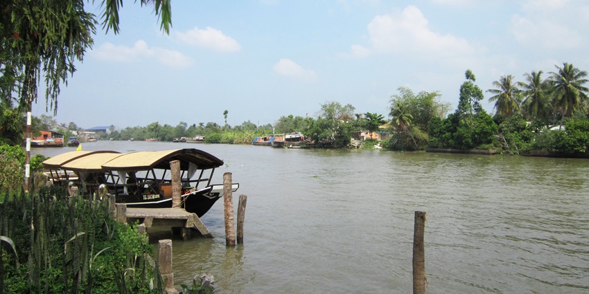 A view of the idyllic Cái Bè featuring sprawling waters decked with a boat and greenery.