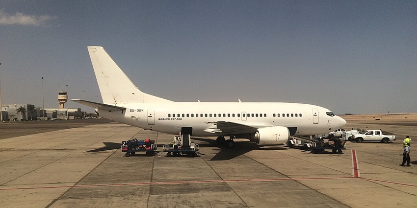 A Boeing aircraft is standing on the tarmac while the ground crew is handling luggage.