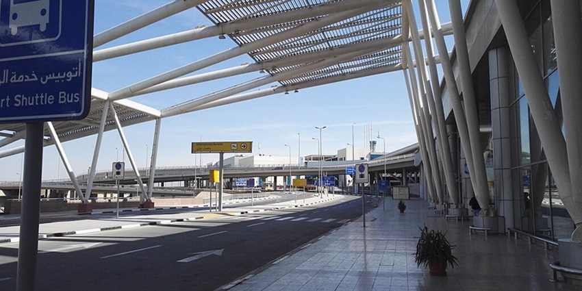 Vehicles are moving through the drop-off area at Cairo Airport Terminal under clear skies.