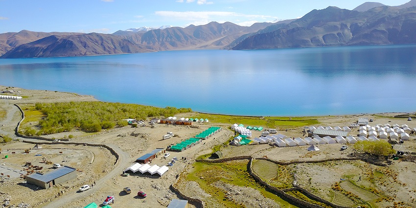 Multiple camps in tent city near the Pangong Lake with vehicles parked and mountains