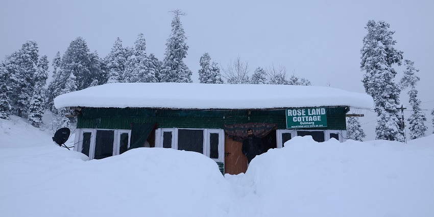 Small Kashmiri-style camping hut with green walls, a sign board and surrounded by snow