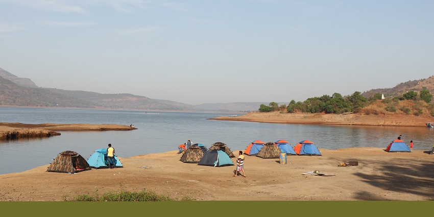 Camp base with multiple tents and people on the Pawna lakeside and distant hills