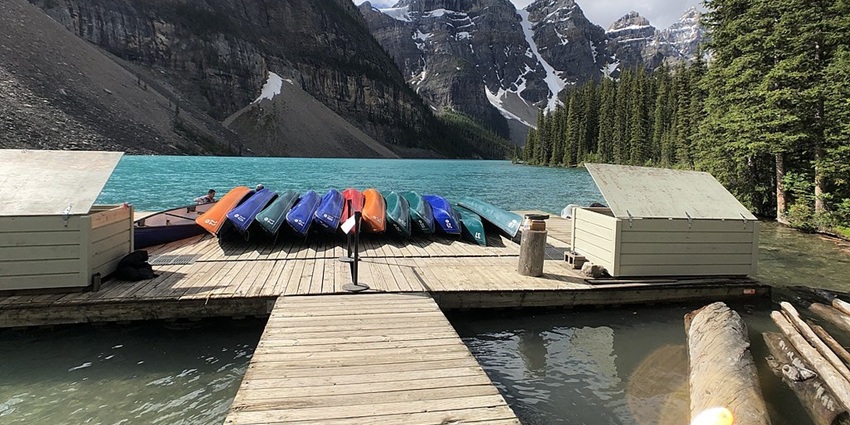 Colourful canoes rest on a wooden dock at Moraine Lake, surrounded by turquoise waters