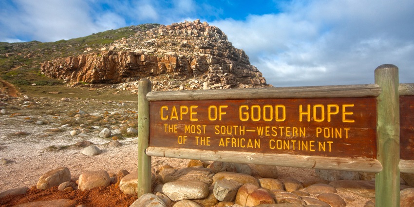 Rocky coastline with blue ocean waves crashing against the cliffs at the Cape of Good Hope.