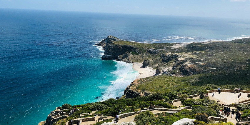 A view of Cape Point's cliffs, blue sea, and lighthouse near the beach in Cape Town.