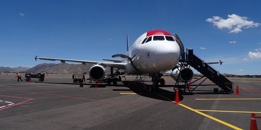 White and red aeroplane parked on the tarmac with workers in the background engaged in various tasks