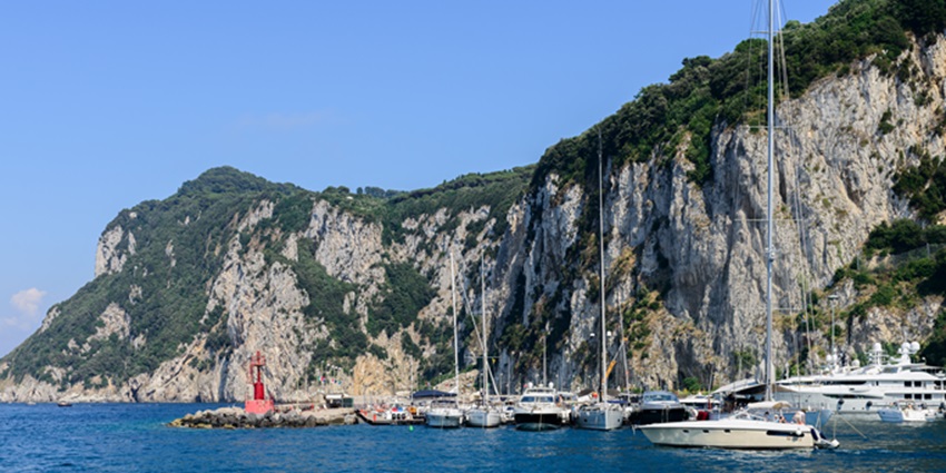 Scenic view of Capri Island with turquoise waters, rugged cliffs, and ships sailing.